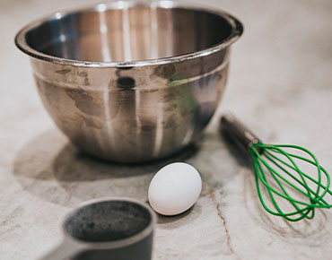 steel bowl, whisk, and egg on white marble counter