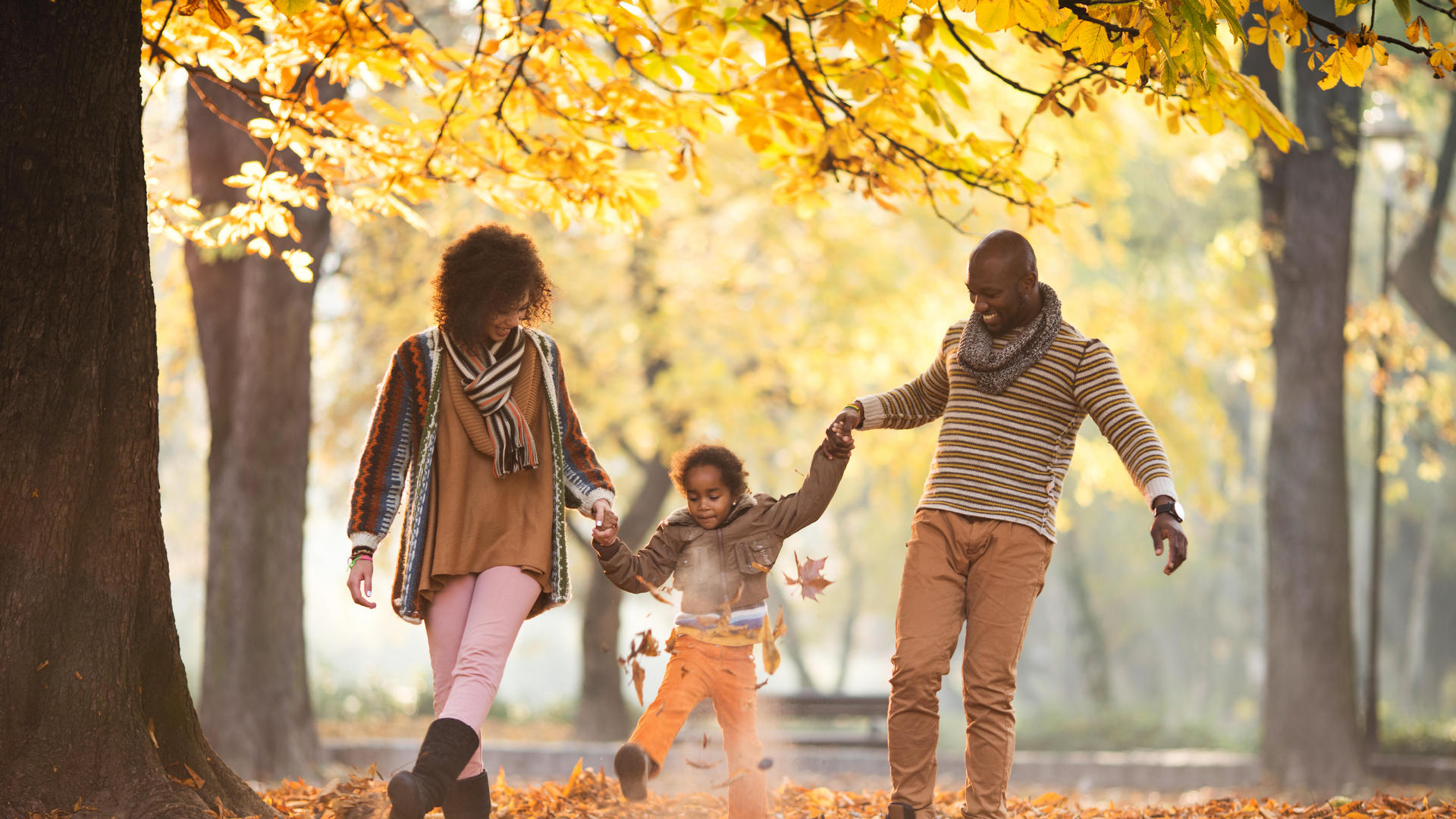 parents swinging daughter in fall leaves