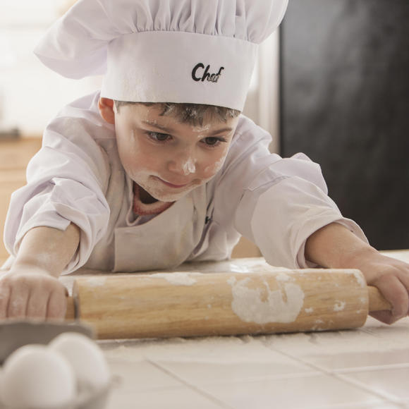 little boy wearing chef hat using rolling pin
